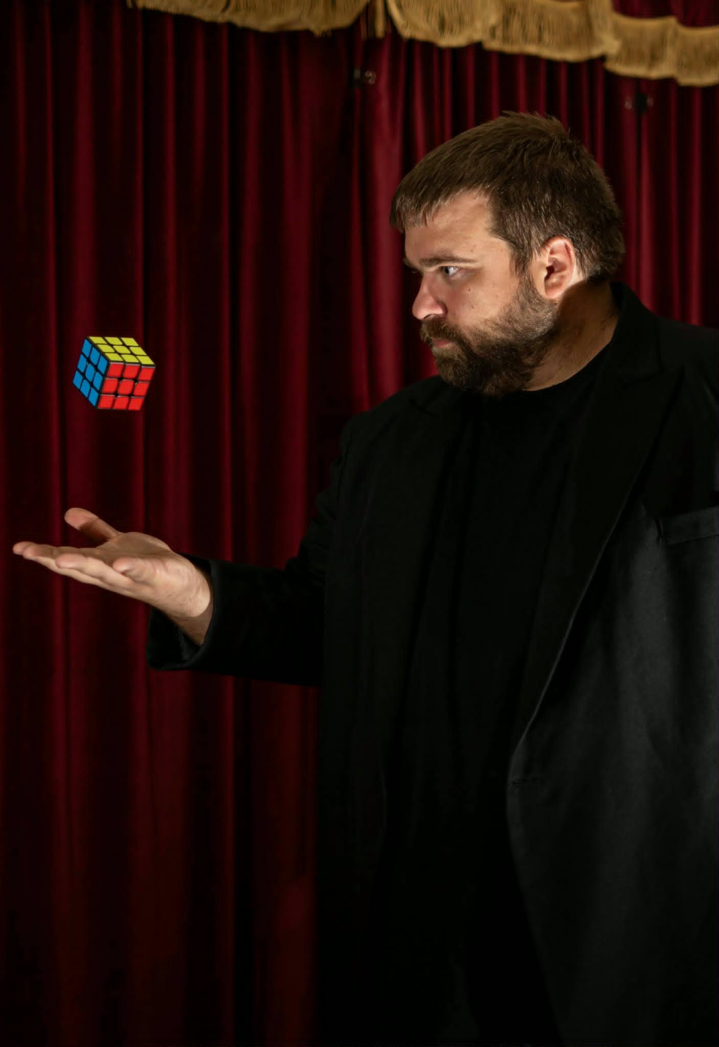 Nate Heater levitating a Rubik's Cube in front of red stage curtains